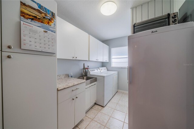 laundry area with sink, light tile patterned floors, independent washer and dryer, cabinets, and a textured ceiling