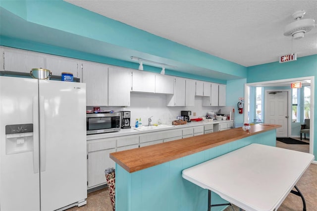 kitchen with white cabinetry, white fridge with ice dispenser, sink, and a textured ceiling