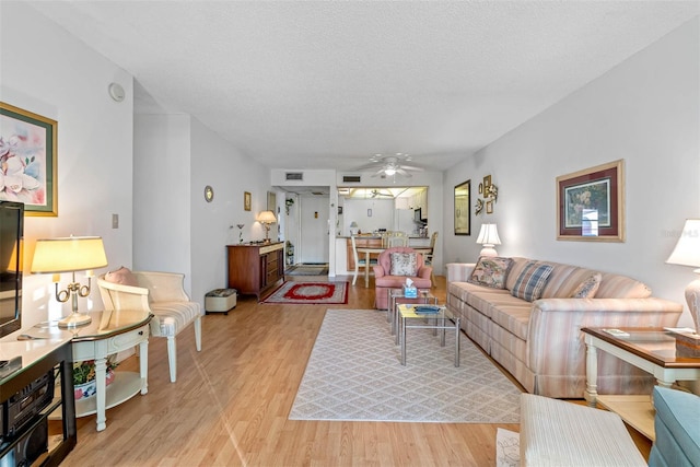 living room featuring a textured ceiling, ceiling fan, and light hardwood / wood-style floors