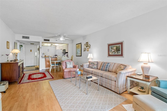 living room featuring light wood-type flooring, ceiling fan, and a textured ceiling