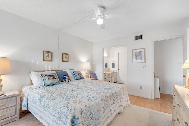 bedroom featuring ceiling fan, light hardwood / wood-style floors, connected bathroom, and a textured ceiling