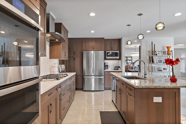 kitchen featuring decorative light fixtures, sink, appliances with stainless steel finishes, an island with sink, and wall chimney exhaust hood