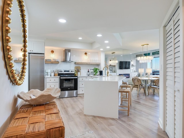 kitchen featuring wall chimney exhaust hood, a breakfast bar, tasteful backsplash, stainless steel appliances, and white cabinets