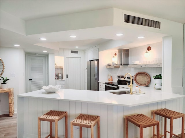 kitchen with a breakfast bar, appliances with stainless steel finishes, ventilation hood, white cabinets, and kitchen peninsula