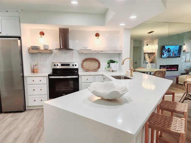 kitchen featuring electric stove, wall chimney range hood, stainless steel refrigerator, and white cabinets