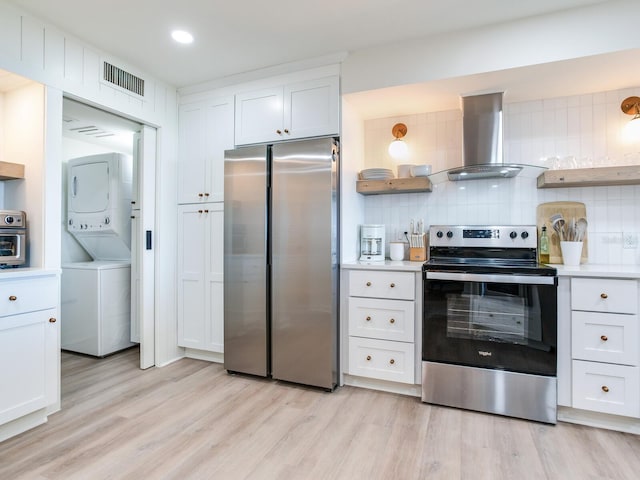 kitchen with stacked washer / drying machine, island range hood, appliances with stainless steel finishes, light hardwood / wood-style floors, and white cabinets