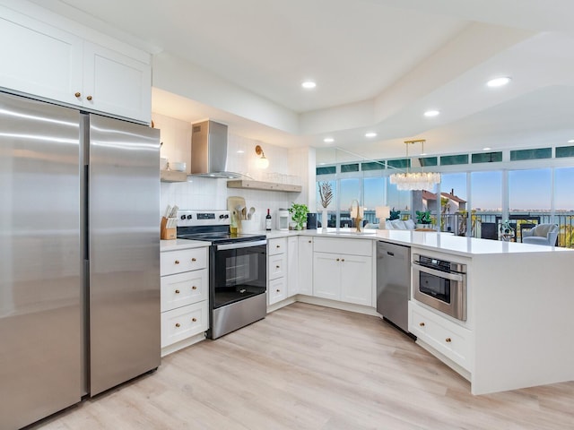 kitchen featuring sink, appliances with stainless steel finishes, white cabinetry, decorative light fixtures, and wall chimney exhaust hood