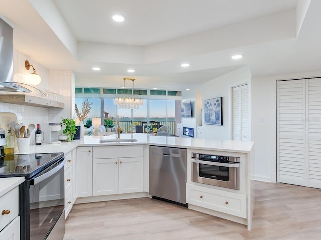 kitchen with white cabinetry, light hardwood / wood-style flooring, appliances with stainless steel finishes, kitchen peninsula, and pendant lighting