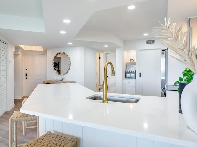 kitchen featuring stainless steel refrigerator, kitchen peninsula, sink, and light hardwood / wood-style flooring