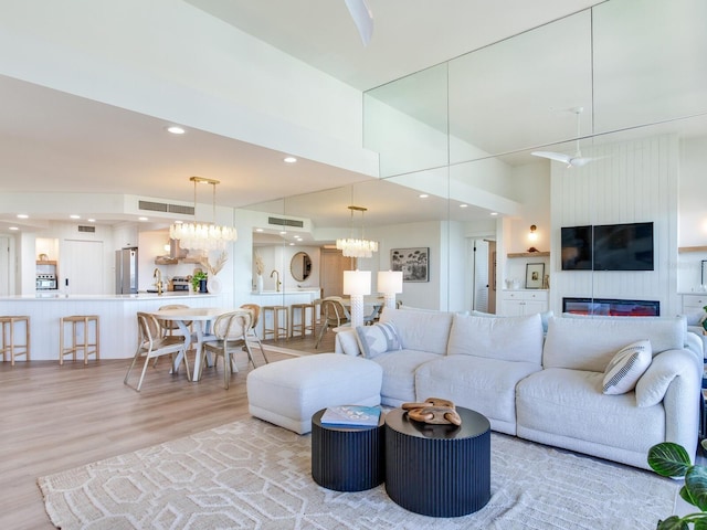 living room featuring an inviting chandelier, a towering ceiling, sink, and light hardwood / wood-style floors