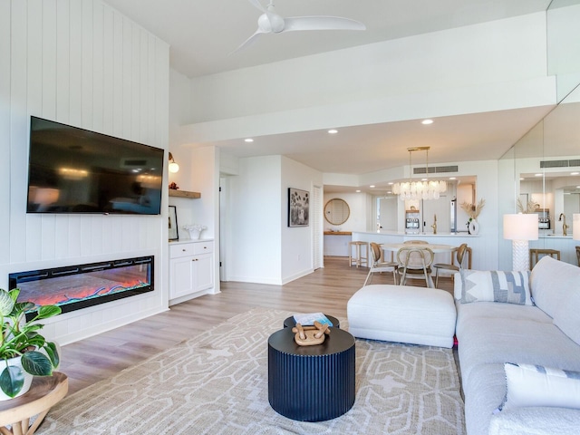 living room with ceiling fan with notable chandelier and light hardwood / wood-style flooring