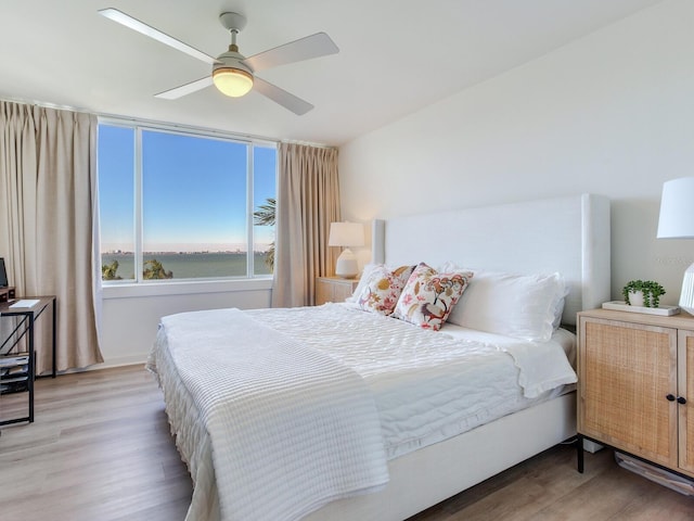 bedroom with hardwood / wood-style flooring, ceiling fan, and a water view