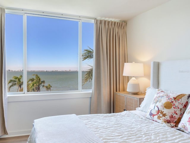 bedroom with hardwood / wood-style floors and a water view