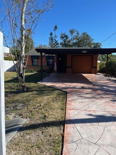 exterior space with concrete driveway, an attached garage, fence, a carport, and a front lawn