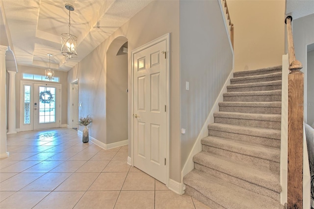 foyer featuring ornate columns, light tile patterned floors, a notable chandelier, a raised ceiling, and a textured ceiling