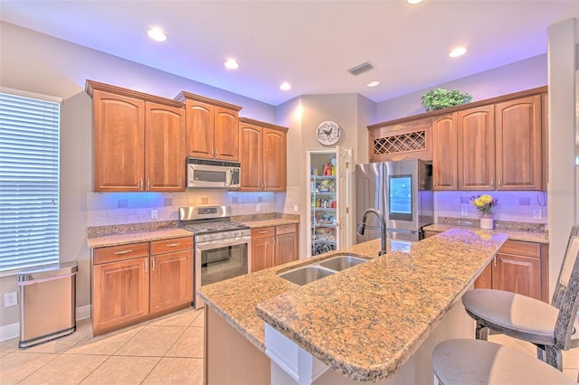 kitchen with a kitchen island with sink, sink, light stone counters, and stainless steel appliances