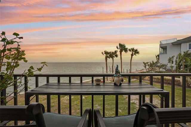 balcony at dusk featuring a water view