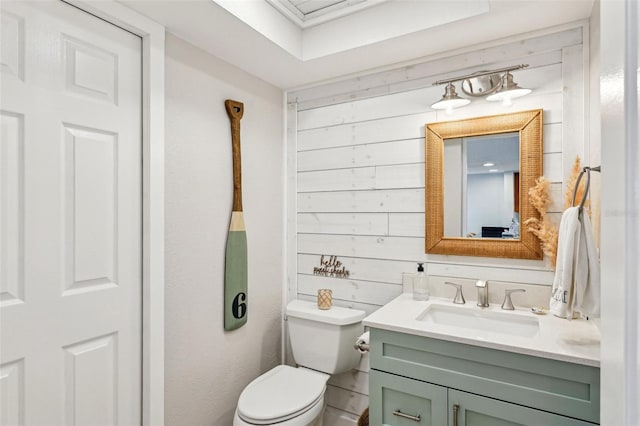 bathroom featuring toilet, wood walls, and vanity