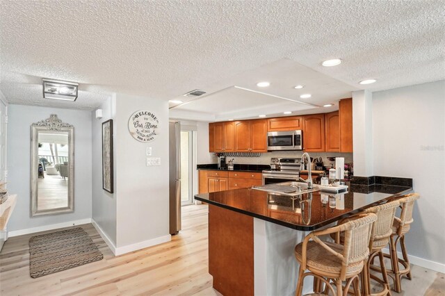 kitchen featuring a kitchen bar, stainless steel appliances, sink, kitchen peninsula, and light wood-type flooring