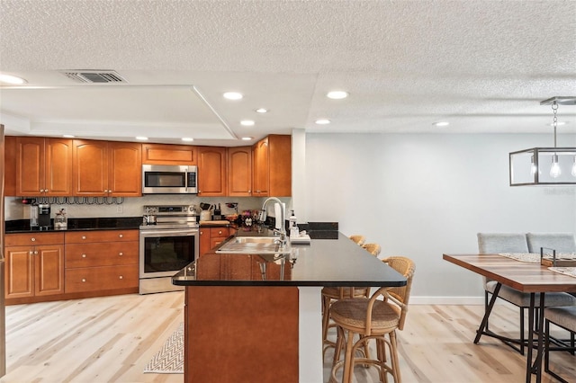 kitchen featuring kitchen peninsula, sink, light wood-type flooring, stainless steel appliances, and a textured ceiling