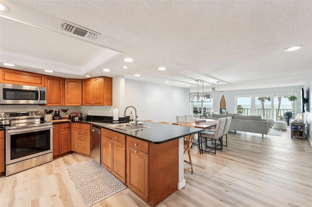 kitchen with sink, a textured ceiling, appliances with stainless steel finishes, and kitchen peninsula