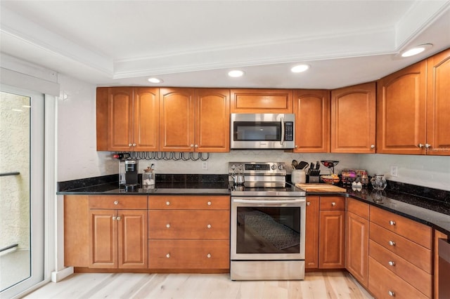 kitchen with light wood-type flooring, stainless steel appliances, dark stone countertops, and a tray ceiling