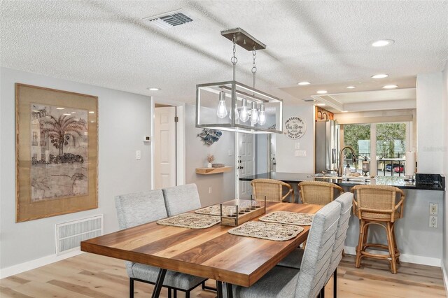 dining space with sink, a textured ceiling, and light wood-type flooring