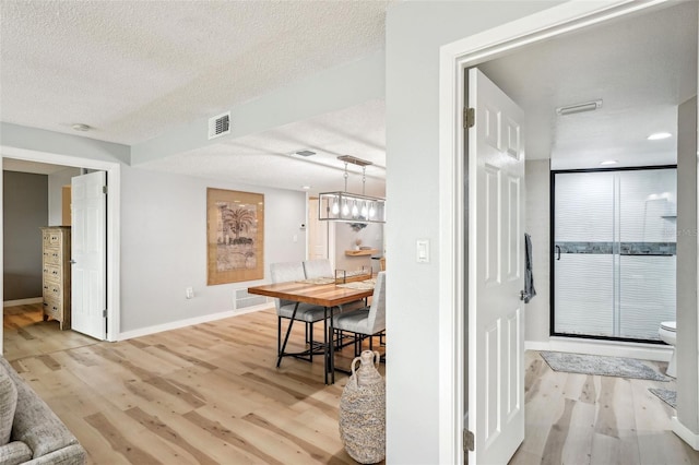 hall featuring a notable chandelier, a textured ceiling, and light hardwood / wood-style flooring