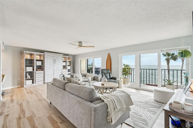 living room with a water view, ceiling fan, a textured ceiling, and light hardwood / wood-style flooring