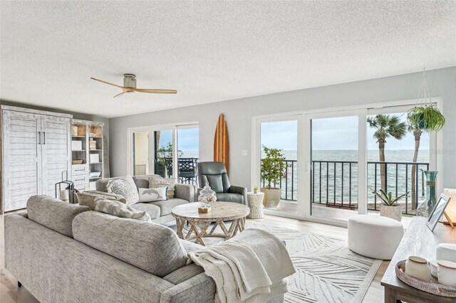 living room with a textured ceiling, ceiling fan, light hardwood / wood-style floors, and a water view