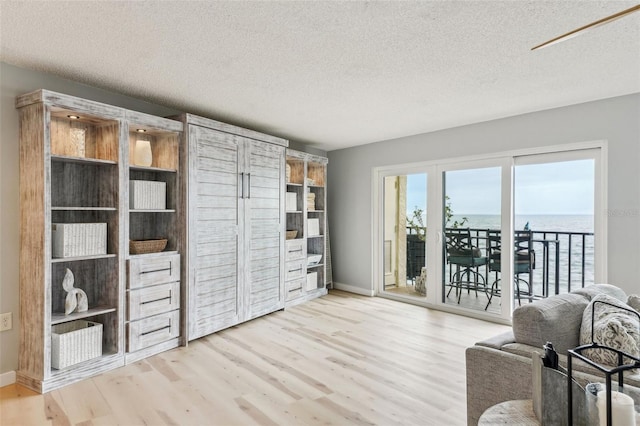 living area featuring a textured ceiling, a water view, and light wood-type flooring