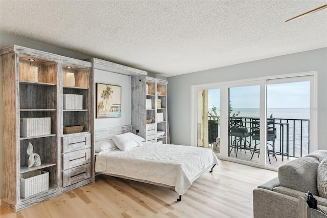 bedroom featuring hardwood / wood-style flooring, access to exterior, a textured ceiling, and a water view