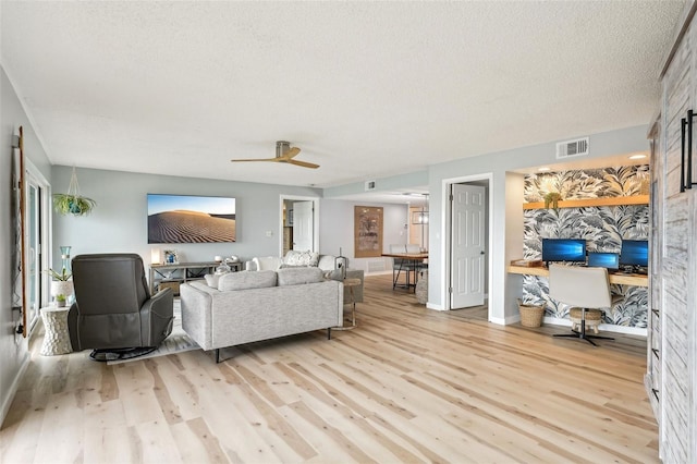 living room featuring ceiling fan, a textured ceiling, and light wood-type flooring