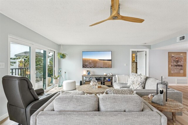 living room with ceiling fan, light wood-type flooring, and a textured ceiling