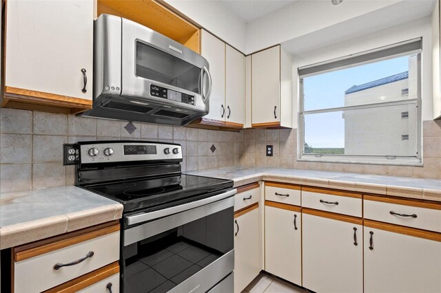 kitchen with white cabinets, appliances with stainless steel finishes, tile countertops, and backsplash