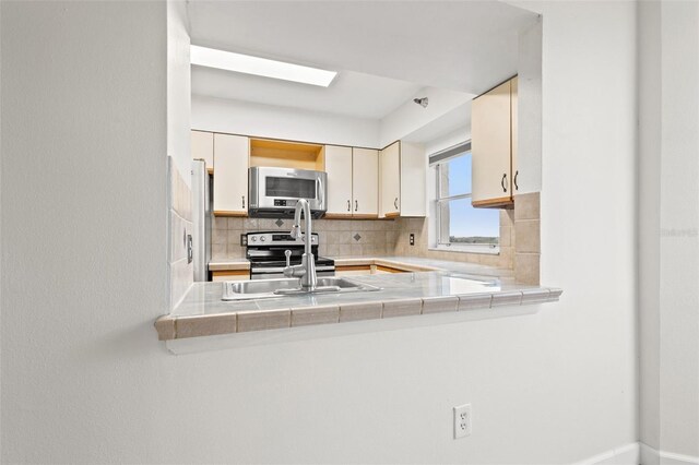 kitchen with tile countertops, stainless steel appliances, tasteful backsplash, cream cabinetry, and sink