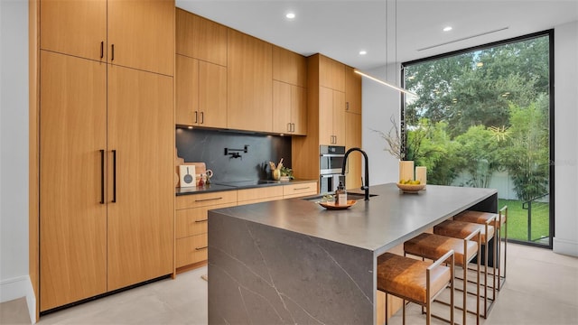 kitchen featuring floor to ceiling windows, a center island with sink, backsplash, a breakfast bar area, and sink