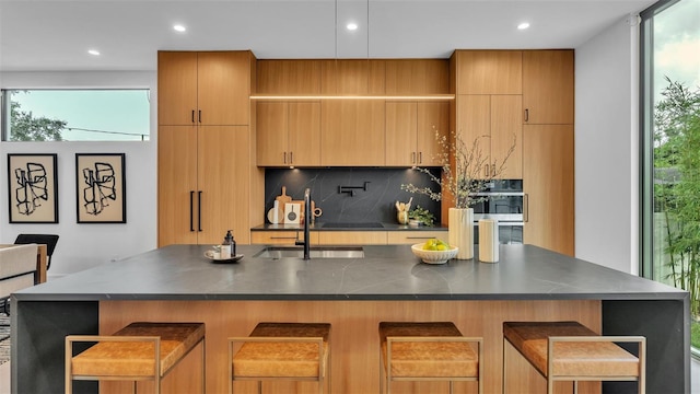 kitchen with a kitchen island with sink, a breakfast bar, decorative backsplash, sink, and decorative light fixtures