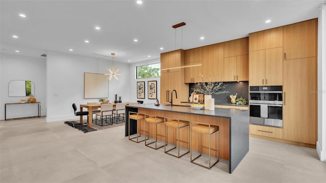 kitchen with decorative light fixtures, a kitchen bar, a large island, stainless steel double oven, and sink