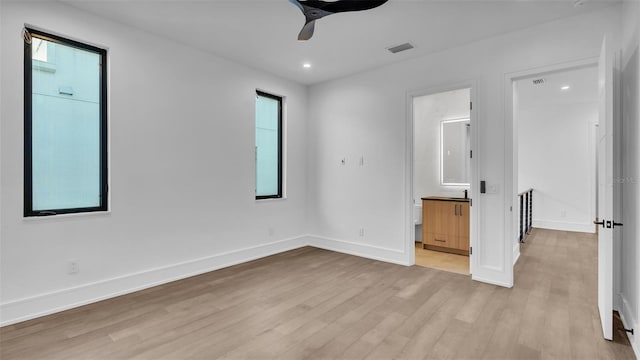 unfurnished bedroom with ensuite bathroom, light wood-type flooring, ceiling fan, and multiple windows