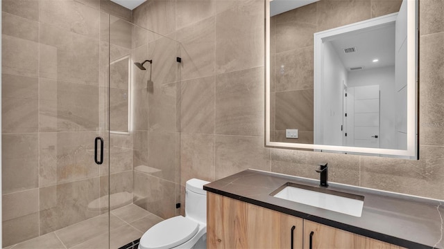 bathroom with tile walls, a shower with shower door, vanity, and toilet