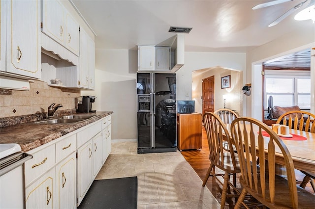 kitchen with black fridge, decorative backsplash, white cabinets, and sink