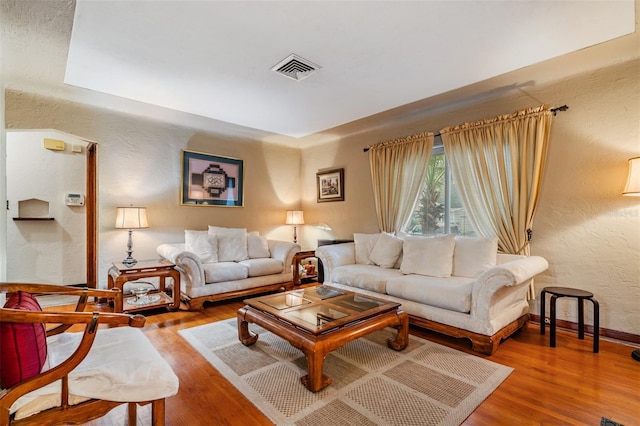 living room featuring a textured wall, wood finished floors, visible vents, and baseboards