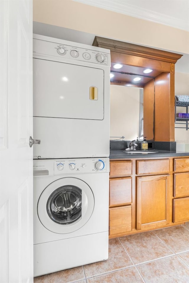 laundry area featuring stacked washer / dryer, sink, crown molding, and light tile patterned flooring