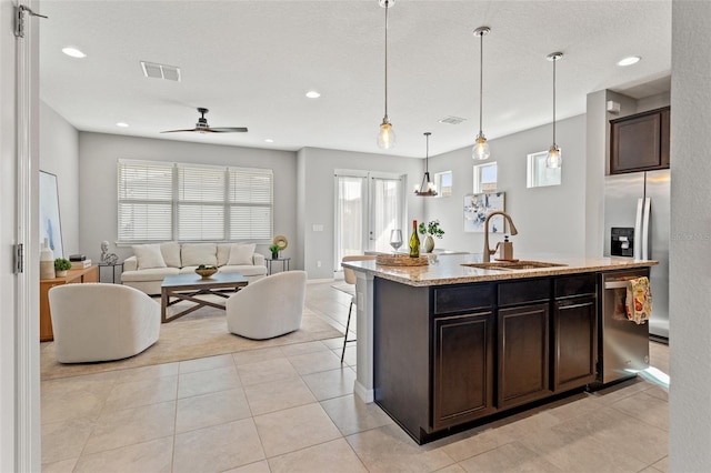 kitchen featuring a kitchen island with sink, stainless steel appliances, dark brown cabinetry, sink, and decorative light fixtures