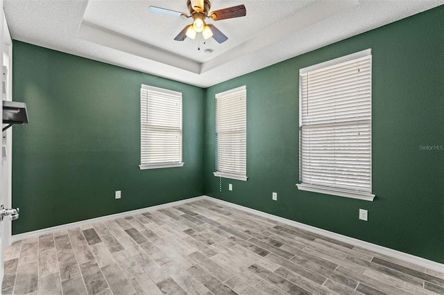 spare room with a raised ceiling, a textured ceiling, ceiling fan, and light hardwood / wood-style floors