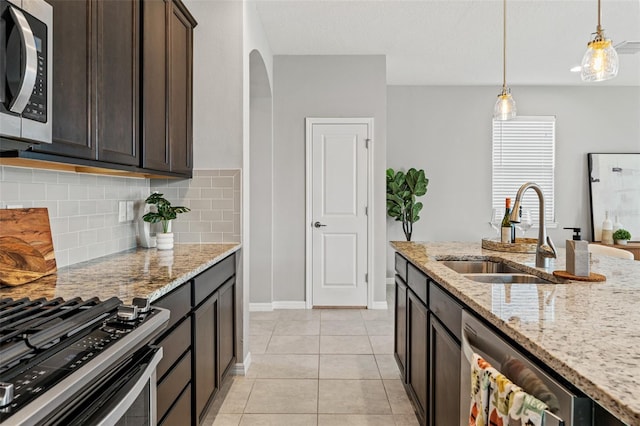 kitchen featuring light stone counters, light tile patterned floors, appliances with stainless steel finishes, dark brown cabinets, and sink