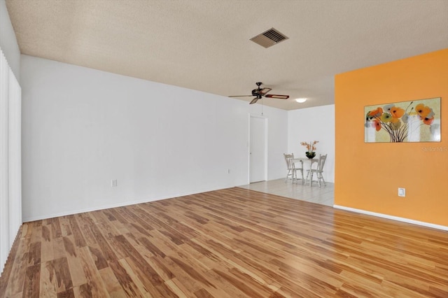 empty room with a textured ceiling, ceiling fan, and light hardwood / wood-style flooring