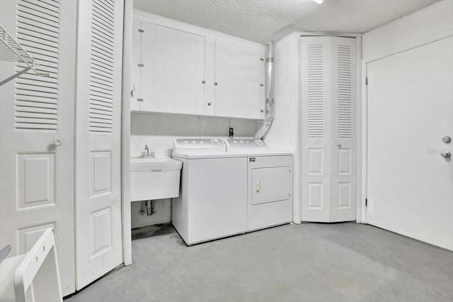 clothes washing area featuring a textured ceiling, cabinets, washing machine and clothes dryer, and sink