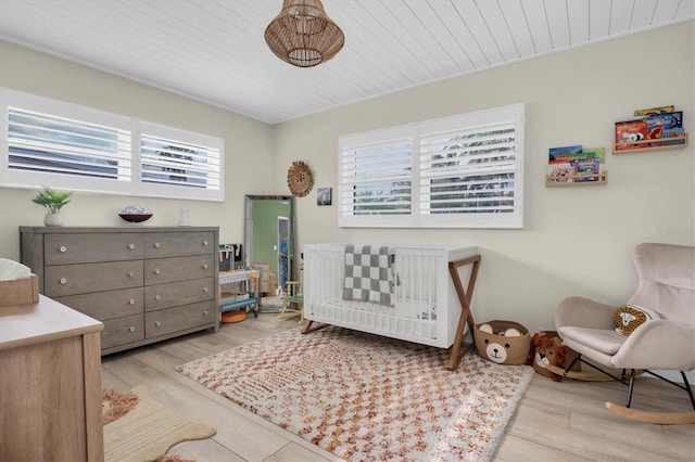 bedroom with light hardwood / wood-style floors, multiple windows, and a crib